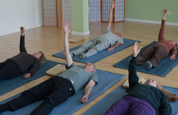 Participants lying on mats with one arm raised during a Feldenkrais Awareness Through Movement lesson.